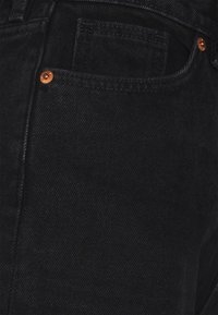 Jean en denim noir avec une texture subtile, doté de rivets en cuivre, d'une poche avant et d'une coupe droite classique.