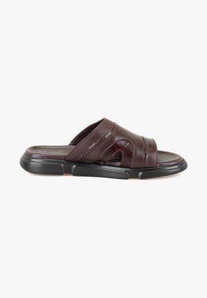 Brown leather slide sandals featuring cut-out designs, a cushioned footbed, and a durable black rubber sole. Flat slip-on design.
