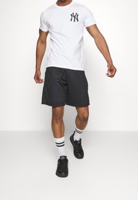 White t-shirt with black NY logo on chest, black textured shorts, white socks with black stripes, and black sneakers.