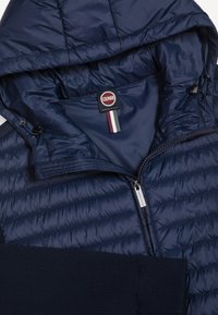 Navyblauw gewatteerd jack met een ritssluiting, verstelbare capuchon met trekkoorden, geribde manchetten en een Colmar Originals-label aan de binnenkant van de kraag.