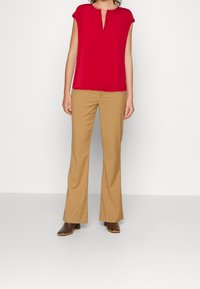 Haut rouge à manches courtes avec un décolleté en V, associé à un pantalon beige évasé et des bottes à talons marron. Tissu lisse et coupe ajustée visibles.