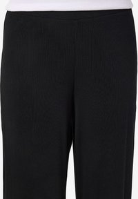 Άτομο που φοράει μαύρο πλεκτό παντελόνι με ίσια γραμμή και λευκό τοπ, εμφανιζόμενο από τη μέση ως τα μέσα μηρού.