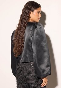 Schwarze Satinbluse mit Puffärmeln und einem cropped Design, kombiniert mit einem strukturierten schwarzen Paillettenrock. Glatte Oberfläche und glänzendes Finish.