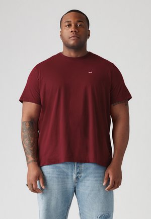 Bordeauxkleurig t-shirt met korte mouwen in een zachte, textuurrijke stof, met een klein wit logo op de borst, gecombineerd met lichtblauwe versleten jeans.