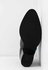 Bottine grise en daim lisse, talon carré et semelle en caoutchouc noire. Accent décoratif bleu près de la cheville.