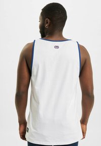Witte tanktop met blauwe randen, gemaakt van katoen, met een ronde onderkant en een klein logopatchje op de rug nabij de hals.