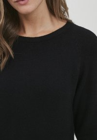 Schwarzer Strickpullover mit rundem Ausschnitt und langen Ärmeln; weiche Textur, taillierte Form und dezente Rippdetails am Kragen.