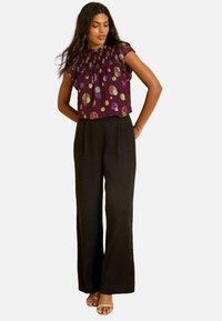 Blusa viola a maniche corte con motivi a pois multicolori, abbinata a pantaloni neri a vita alta e a gamba larga e sandali color carne.