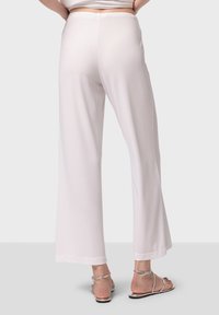 Pantalons larges en tissu beige clair, présentant une texture lisse et une taille simple. Associés à des sandales à lanières argentées.
