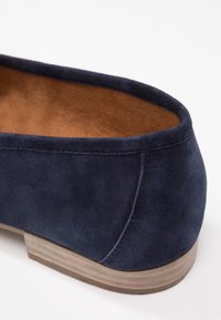 Navy zamszowe buty o gładkiej fakturze, zaokrąglonym kształcie i jasnobrązowej drewnianej podeszwie. Posiadają przeszywaną szew wzdłuż krawędzi.