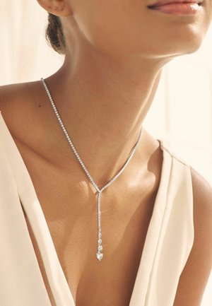 Silverhalsband med länkade stenar i en Y-formad design, med ett hängande hänge och liten hjärtformad detalj. Texturerad yta, elegant utseende.