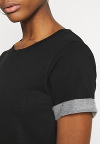 Czarna krótka koszulka z krótkim rękawem, okrągłym dekoltem i podwiniętymi szarymi mankietami. Miękka tekstura z casualowym stylem.