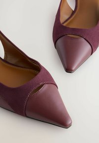 Burgundy kengät, joissa on terävä kärki ja avointa takaa, valmistettu mokasta ja nahasta, tarjoavat leikattua yksityiskohtaa sekä sileän, kiiltävän pinnan.
