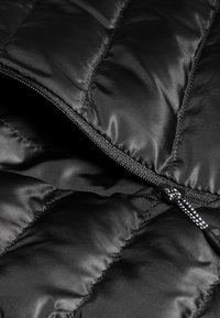 Zwarte pufferjas in close-up, met een geborduurd patroon, gladde, glanzende stof en een ritsluiting met contrasterende zwarte hardware-accenten.
