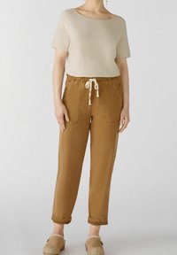 Haut beige à manches courtes associé à un pantalon marron à taille élastique avec deux poches avant et un cordon de serrage, des manches roulées et une coupe décontractée.