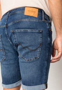Blå denimshorts med ett lädermärke med varumärkeslogotyp, uppvikt fåll och bakfickor med kontrasterande sömmar.