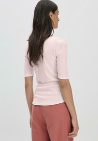 Lichtroze, aangesloten top met korte mouwen, gladde textuur en ronde zoom, gecombineerd met losse, roestkleurige broeken.