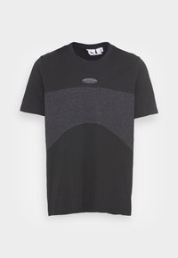 Černé tričko s světlomodrým panelem přes hruď. Uprostřed se nachází kulaté logo a má krátké rukávy. Materiál je směs bavlny.