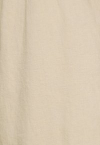 Tissu beige clair avec une surface lisse et légèrement texturée. Il présente une couleur uniforme et un motif de tissage subtil.
