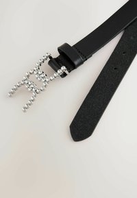 Black leather belt featuring a rhinestone-accented buckle shaped like an abstract figure, with a matte texture and polished accents.