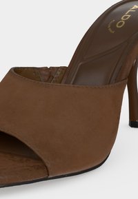 Mule en daim marron à talon haut avec bout ouvert et marquage "ALDO" sur la semelle intérieure matelassée.