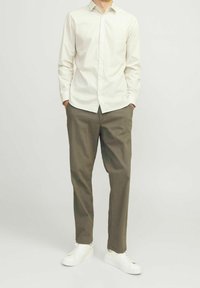 Ein weiß- und grün gestreiftes Hemd mit Knöpfen, beige Hose und weiße Sneakers. Gerades Design mit einer glatten Textur und ohne sichtbare Muster.