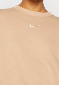 Béžová mikina s kulatým výstřihem, vyrobená z měkké bavlny, s mal�ým bílým logem Nike vyšitým na prsou.