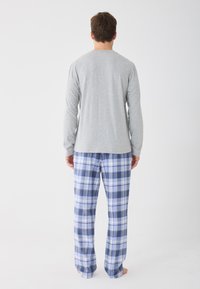 Sivý top s dlhým rukávom v kombinácii s modro-bielymi kockovanými pyžamovými nohavicami vyrobenými z mäkkej tkaniny. Nohavice majú elastický pás pre väčšie pohodlie.