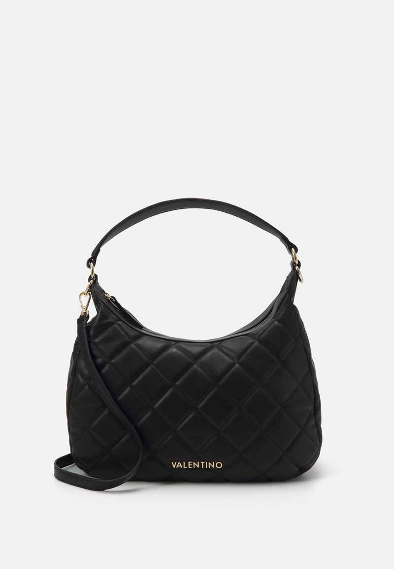 Black quilted handbag with a structured shape, featuring a top zipper, short handle, and gold logo detail on the front. Smooth texture.