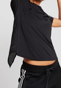 Top deportivo negro de manga corta, con paneles de malla en los hombros y los laterales para mayor transpirabilidad. Tejido suave y ligero.