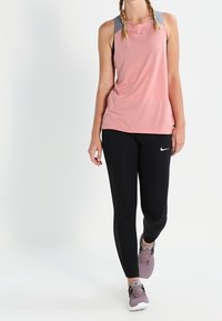 Lyserød ærmeløs træningsbluse med grå detaljer, parret med sorte leggings med en struktureret panel, og lyse lilla træningssko.