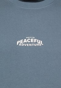 Blue cotton sweatshirt with round neckline, featuring white text: "Ready for a new PEACEFUL ADVENTURE." Soft texture and casual design.