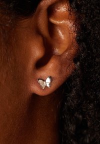 Boucle d'oreille en argent en forme de papillon fixée au lobe de l'oreille. Surface lisse avec des accents réfléchissants, forme d'aile complexe et finition polie.