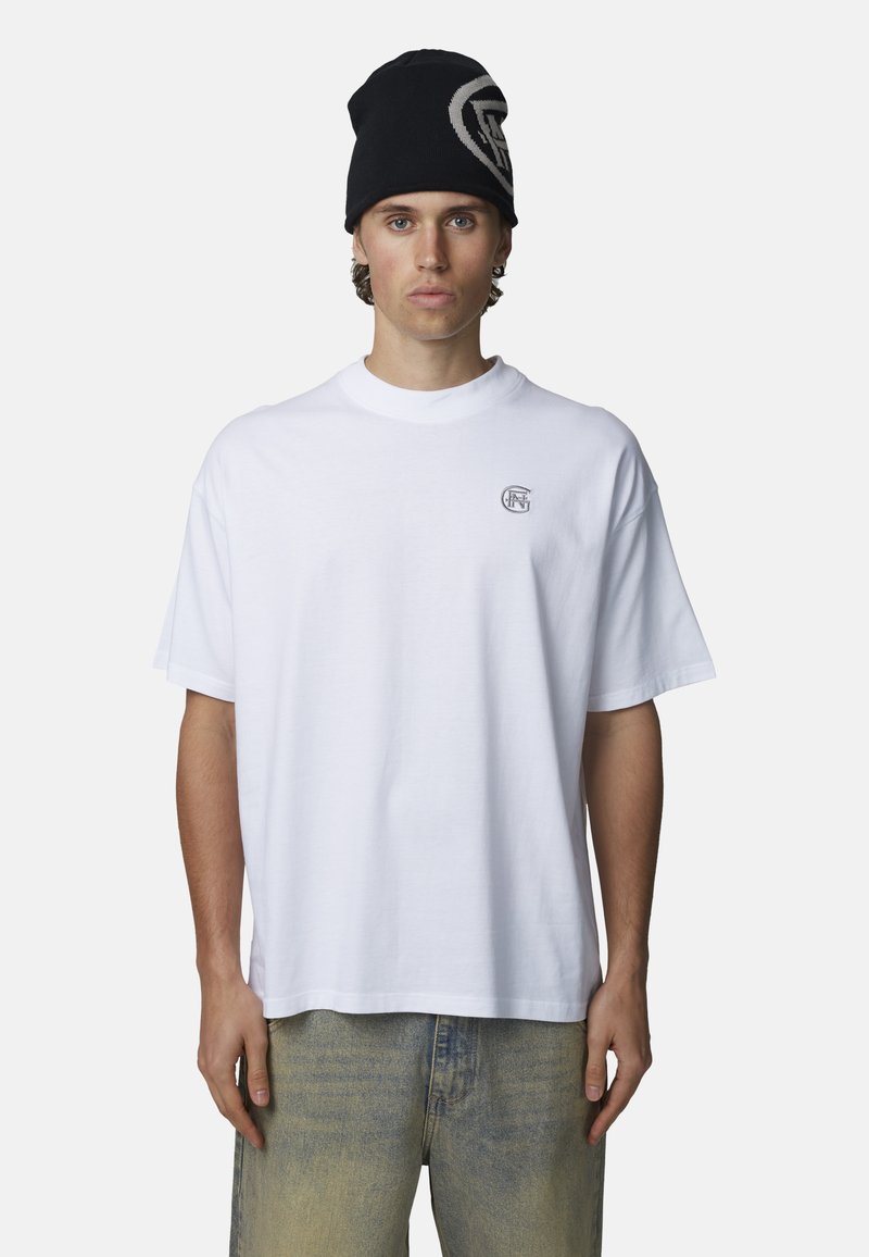 Witte katoenen T-shirt met een ontspannen pasvorm, korte mouwen en een klein logo op de borst. Gecombineerd met lichtblauwe, vervaagde spijkerbroeken en een zwarte beanie.