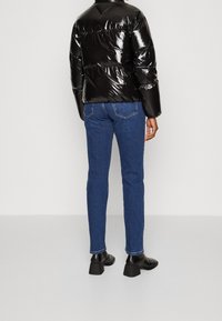 Sort glansende puffjakke, blå slim-fit jeans og sorte hæl ankle boots. Jakken har en kort længde og en puffy tekstur.