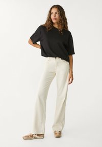 Svart löst sittande t-shirt, off-white vida byxor och bruna sneakers. Mjukt tyg, minimala sömmar och enkel design med neutrala färger.