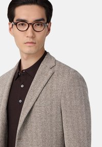 Blazer i houndstooth-mönster, ljusbrun med en texturerad yta, kombinerad med en mörkbrun pikétröja med knäppt krage.