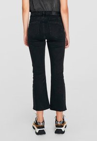 Jeans svasati in denim nero con vita alta, orlo grezzo e tasche posteriori, abbinati a sneakers grigie e nere.