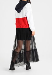 Kurtka w blokach kolorystycznych z białymi, czerwonymi i granatowymi panelami; zestawiona z długą czarną spódnicą z tiulu i botkami, prezentując warstwowe tekstury.