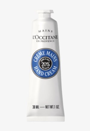 Crème pour les mains L'Occitane dans un tube blanc de 30 ml, avec une étiquette circulaire bleue indiquant "20% beurre de karité" et le texte "CRÈME MAINS". Bouchon à clapet.