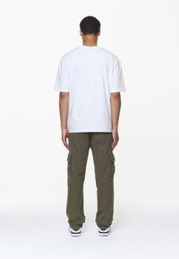 Bílá bavlněná tričko s krátkými rukávy, spárované se zelenohnědými cargo kalhotami se bočními kapsami a volným střihem, obuté s černobílými teniskami.