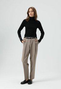 Zwarte coltrui met lange mouwen en knoopaccenten, gecombineerd met beige hoge taillebroek en zwarte loafers, met een getailleerde pasvorm.