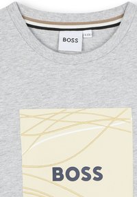 T-shirt en coton gris avec un col rond, un graphique rectangulaire crème avec des lignes abstraites, et "BOSS" imprimé en lettres noires en gras.