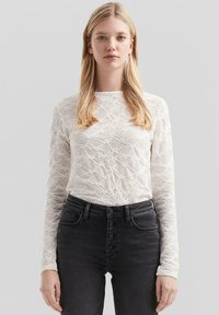 Witte kanten top met lange mouwen, een gestructureerd patroon, ronde halslijn en een getailleerd ontwerp, gecombineerd met hoge taille zwarte jeans met knopen.