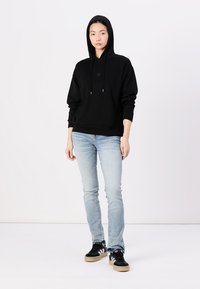 Sweat à capuche noir avec une poche avant et des cordons de serrage ajustables, associé à un jean ajusté bleu clair et des baskets noires avec des semelles crème.