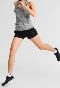 Graues und schwarzes sportliches Tanktop mit strukturiertem Muster, kombiniert mit schwarzen Shorts. Schwarze Sneakers mit weißen Akzenten. Laufpose.
