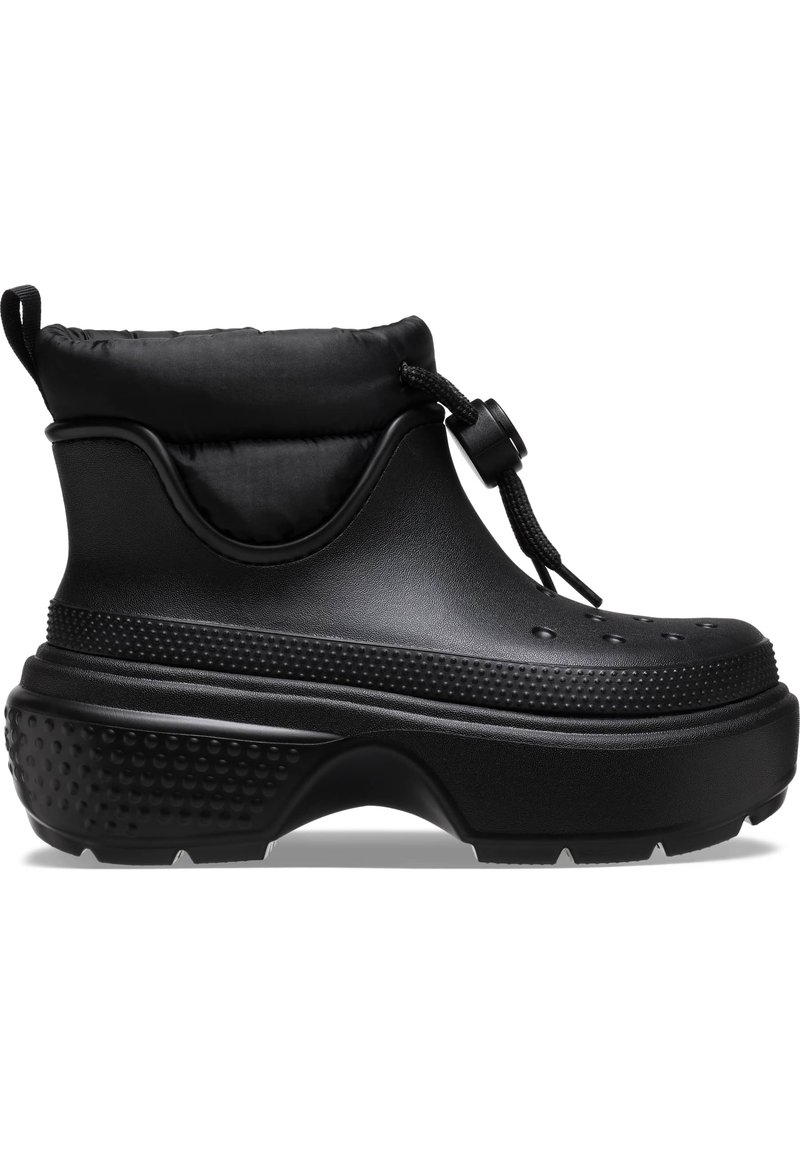 Botas negras hasta el tobillo con un puño acolchado, hechas de un material similar al caucho. Presentan acentos texturizados y una suela gruesa con dibujo para un mejor agarre.