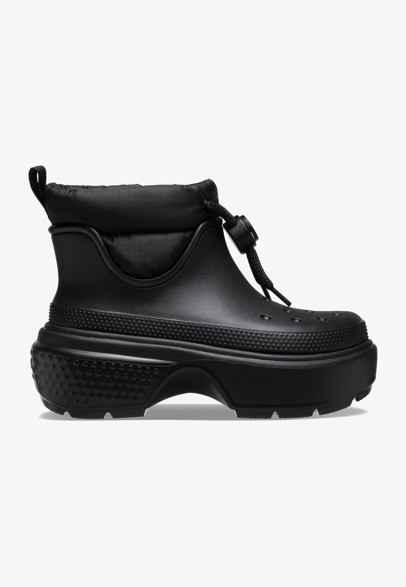 Botas negras hasta el tobillo con un puño acolchado, hechas de un material similar al caucho. Presentan acentos texturizados y una suela gruesa con dibujo para un mejor agarre.