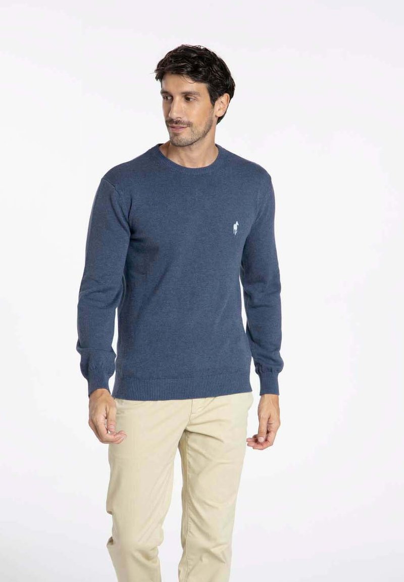 Pull marine en tricot, avec un col rond, des poignets et un ourlet côtelés. Logo blanc notable sur la poitrine gauche.