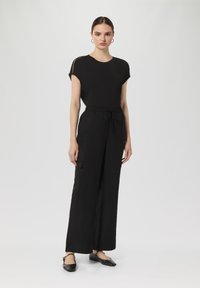 Schwarzer Jumpsuit mit kurzen Ärmeln, elastischem Bund, weitem Bein und seitlichen Taschen. Besitzt eine glatte Textur und ein minimalistisches Design.